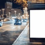 pannello pubblicitario sul marciapiede di una strada trafficata di sera